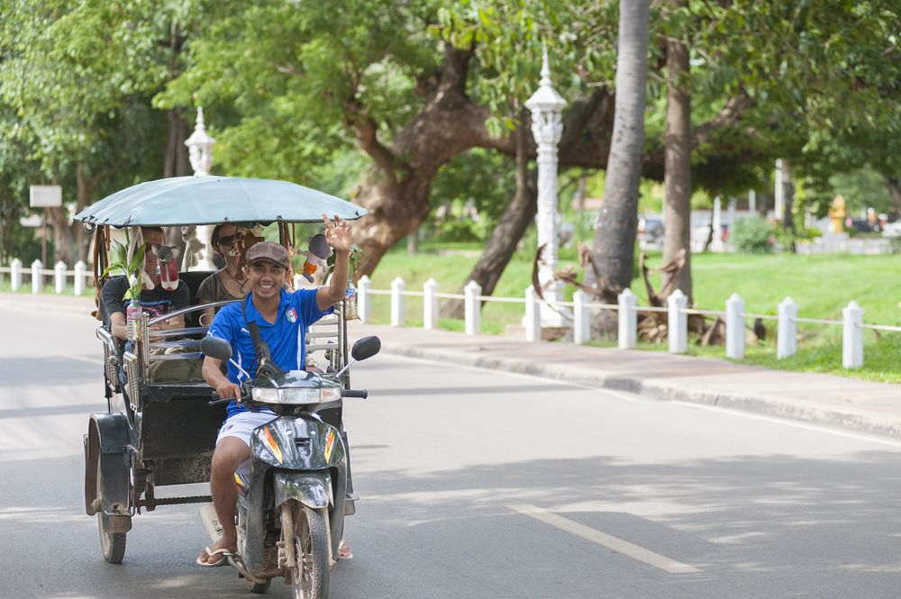 A tuktuk driver with a big smile drives tourists on the street of Siem Reap